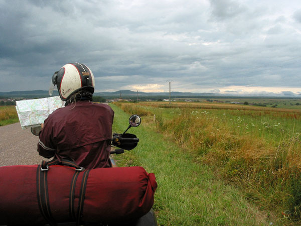 Sylvia stopped on het motorcycle, map in hand, dark clouds in the distance