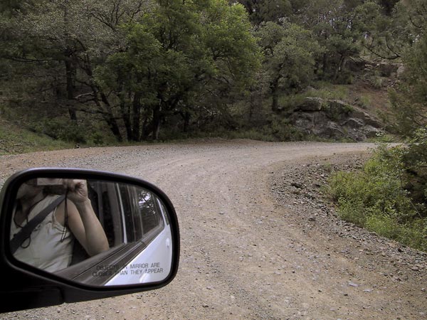 Photographer in car mirror, unpaved road
